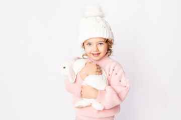 happy child girl on a white isolated background with a Christmas bunny in her hands in a pink sweater and hat smiling, space for text
