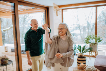 Senior couple in love dancing together in their modern living room.