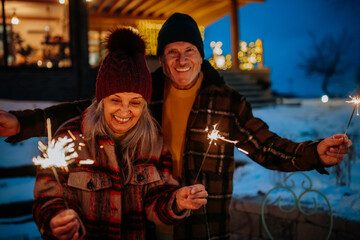 Fototapeta na wymiar Happy senior couple celebrating new year with sparklers, enjoying winter evening.