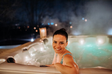 Young woman enjoying outdoor bathtub in her terrace during cold winter evening.
