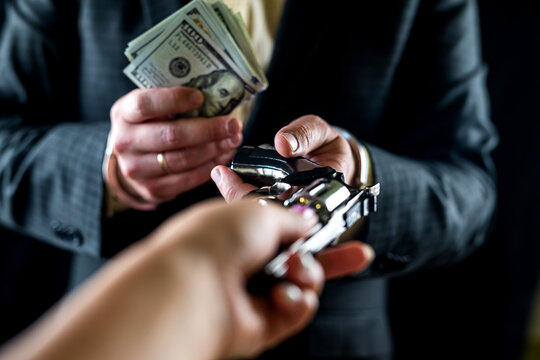 cropped photo of man in suit handing black gun and wad of dollars isolated on black background