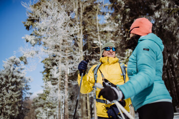 Senior couple skiing together in the middle of forest, having break.