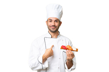 Young caucasian chef holding a sushi over isolated background with surprise facial expression