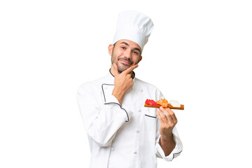Young caucasian chef holding a sushi over isolated background happy and smiling