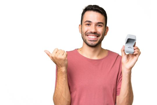 Young handsome caucasian man holding a engagement ring over isolated background pointing to the side to present a product - Powered by Adobe