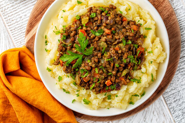 Lentil and vegetable stew over mashed potatoes with parsley.  Raw lentils on background. Healthy vegan food concept. Top view.