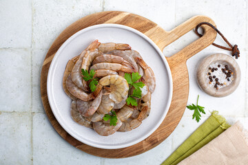 Top view of raw fresh headless shrimp tails or prawns, uncooked jumbo seafood on a white plate,...