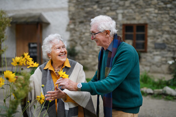 Happy senior couple at autumn city walk, posing with flowers.