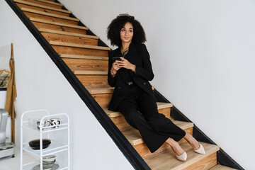 Young businesswoman using cellphone while sitting on stairs at home