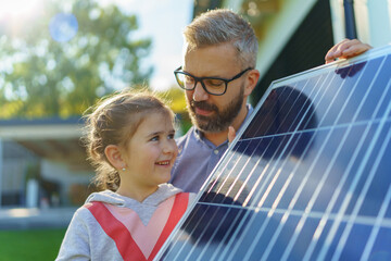 Father with his little daughter near their house with solar panels. Alternative energy, saving...