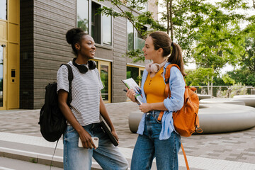 Young multiracial women talking while standing by campus outdoors
