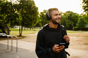 Young white man using mobile phone while listening to music in park