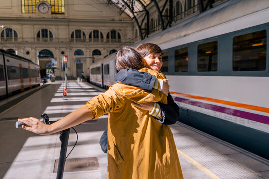 Happy woman with push scooter embracing friend at station