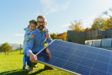 Father with his little daughter catching sun at solar panel,charging at their backyard. Alternative...