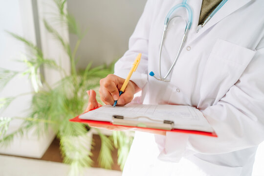 Doctor Wearing Lab Coat Writing Prescription At Clinic