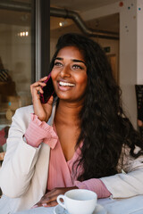 Young indian woman drinking coffee and talking on mobile phone