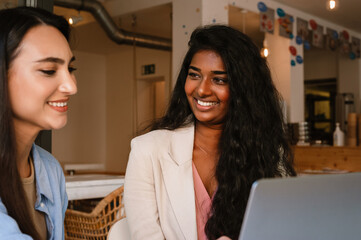 Young indian women talking while working with laptop in cafe