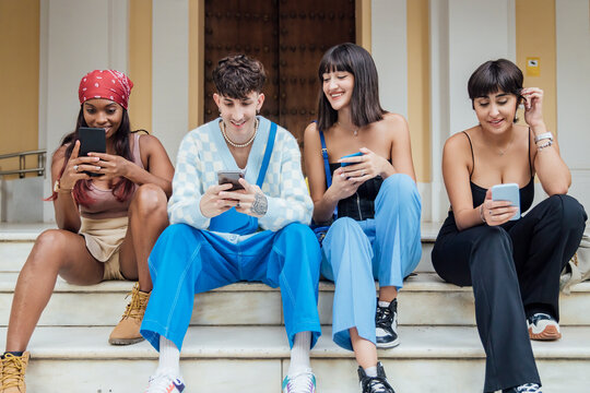 Happy friends using smart phones on staircase in front of door