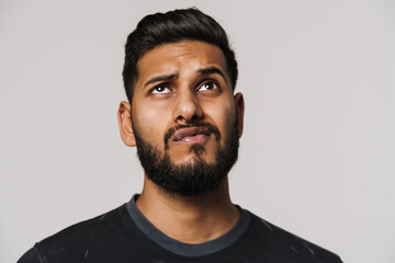 Obraz premium Puzzled indian man with beard grimacing and looking upward