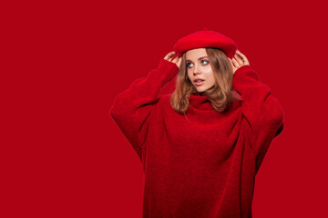 Fototapeta premium Beautiful girl in red clothes isolated on colorful red background. Isolated. Cute girl wears a beret with delight looks away from amazement or from a pleasant surprise 