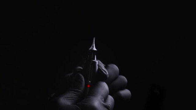 Hands of a master of permanent make-up of eyebrows, lips and eyelashes in black sterile gloves. Close-ups of how the master inserts the permanent makeup cartridge into the tattoo machine with