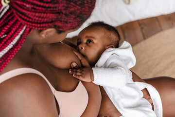 Young african american woman breastfeeding her baby in bedroom - Powered by Adobe