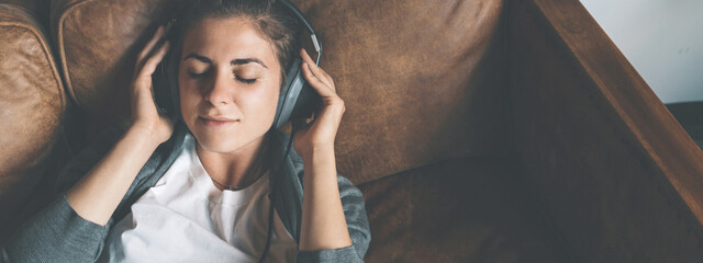 Handsome young girl listening to music from headphones with pleasure at coworking office, lying on...