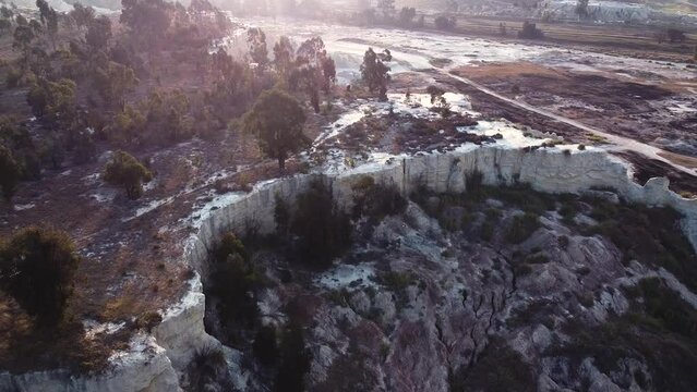 Aerial drone shot tracking backwards over an old eroded mine dump as the golden rays from the morning sunrise casts a shadow on what remains of the history of the lucrative gold rush, South Africa 