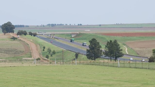 A shot overlooking agricultural farmland on to the N4 National highway with a number of passenger vehicles, coal and logistics trucks passing by travelling, Mpumalanga, South Africa