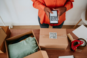 Businesswoman scanning QR code on package at desk