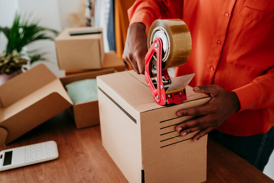 Hands Of Businesswoman Sealing Packages With Tape At Desk