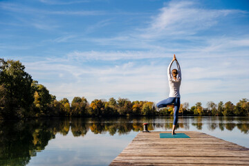 Woman practicing yoga on jetty at lake