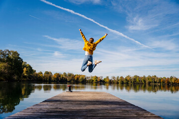 Carefree woman jumping on jetty under vapor trail