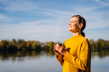 Smiling woman with coffee cup standing under sky