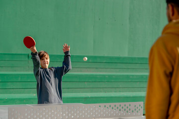 Boy playing table tennis with father in front of green wall