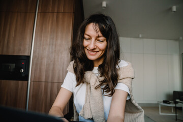Fototapeta na wymiar Young white happy woman smiling and sitting with laptop by table at home