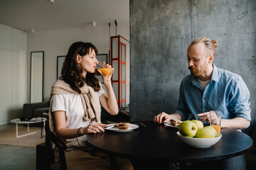 Young white couple sitting by table while having breakfast at home