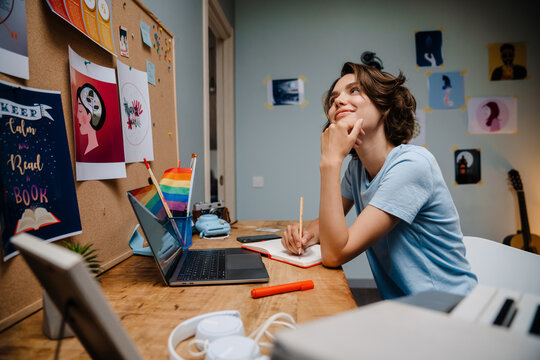 Young white woman writing down notes while working with laptop