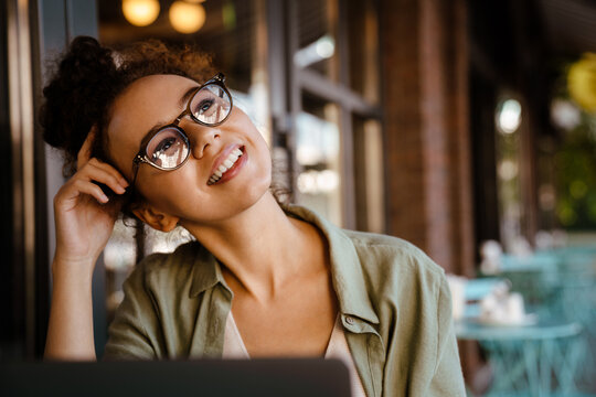 Hispanic woman in eyeglasses working with laptop while sitting at cafe