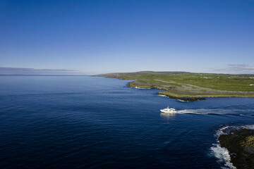 Small ferry boat leaving Doolin harbor on the way to Aran islands, Ireland. Travel and tourism industry. Warm sunny day with blue sky and ocean surface. Cruise boat in the ocean. Irish coastline.