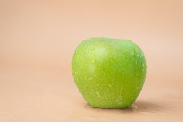 Water splashing on fresh green apple on beige background.