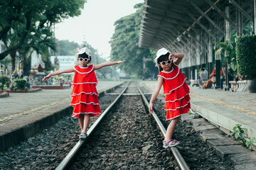 Two little sisters in red dresses walk along the train tracks in summer. Sisters were walking on...