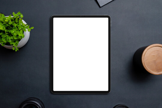 Tablet mockup on black table surrounded by objects. Isolated, transparent display in white for app or web design promotion. Top view, flat lay composition