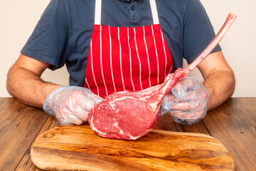 Professional butcher in red and white stripe apron showing high quality tomahawk steak over a...