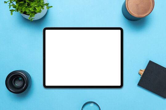 Tablet with isolated, transparent display on blue table. Top view, flat lay composition. The plant, lens, box, magnifying glass and table beside