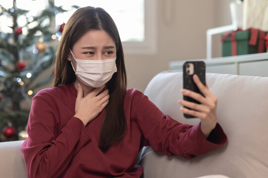 Young Asian Woman Using Smartphone Connect Video Call Talking With Doctor From Hospital Consult About Sickness Symptom During Home Isolation In Christmas Holiday. Health Care And Telehealth Technology