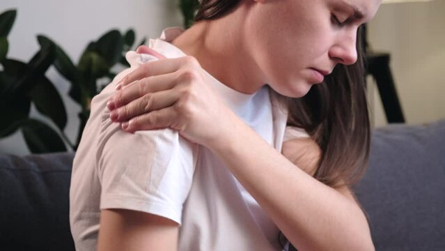 Arm injury, shoulder and forearm pain, people with body muscle problems, healthcare and medicine concept. Close up of upset young woman sitting on couch doing massage in shoulder with other hand