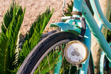 Front wheel of an old turquoise bicycle with one headlight