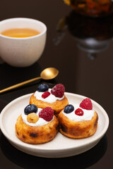 Cheese pancakes with blueberries, raspberries and sour cream on a plate.