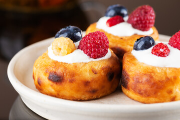 Russian breakfast cheese pancakes or syrniki with blueberries, raspberries and sour cream.